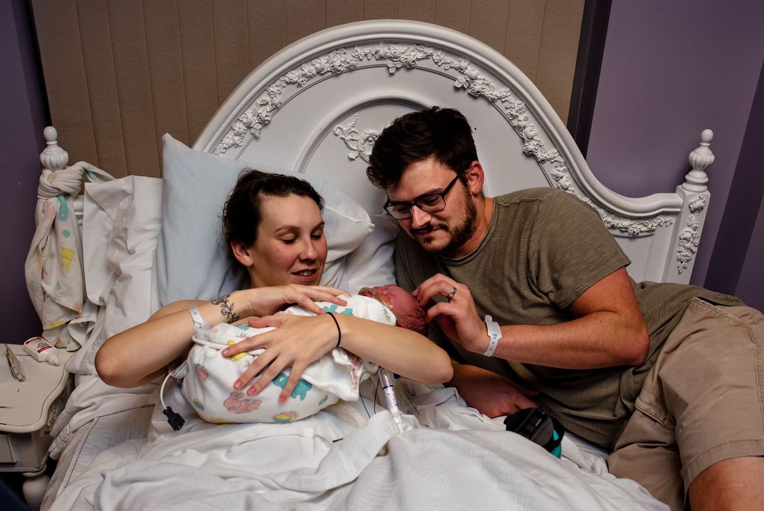 Intimate moment showing new parents bonding with infant on ornate bed.