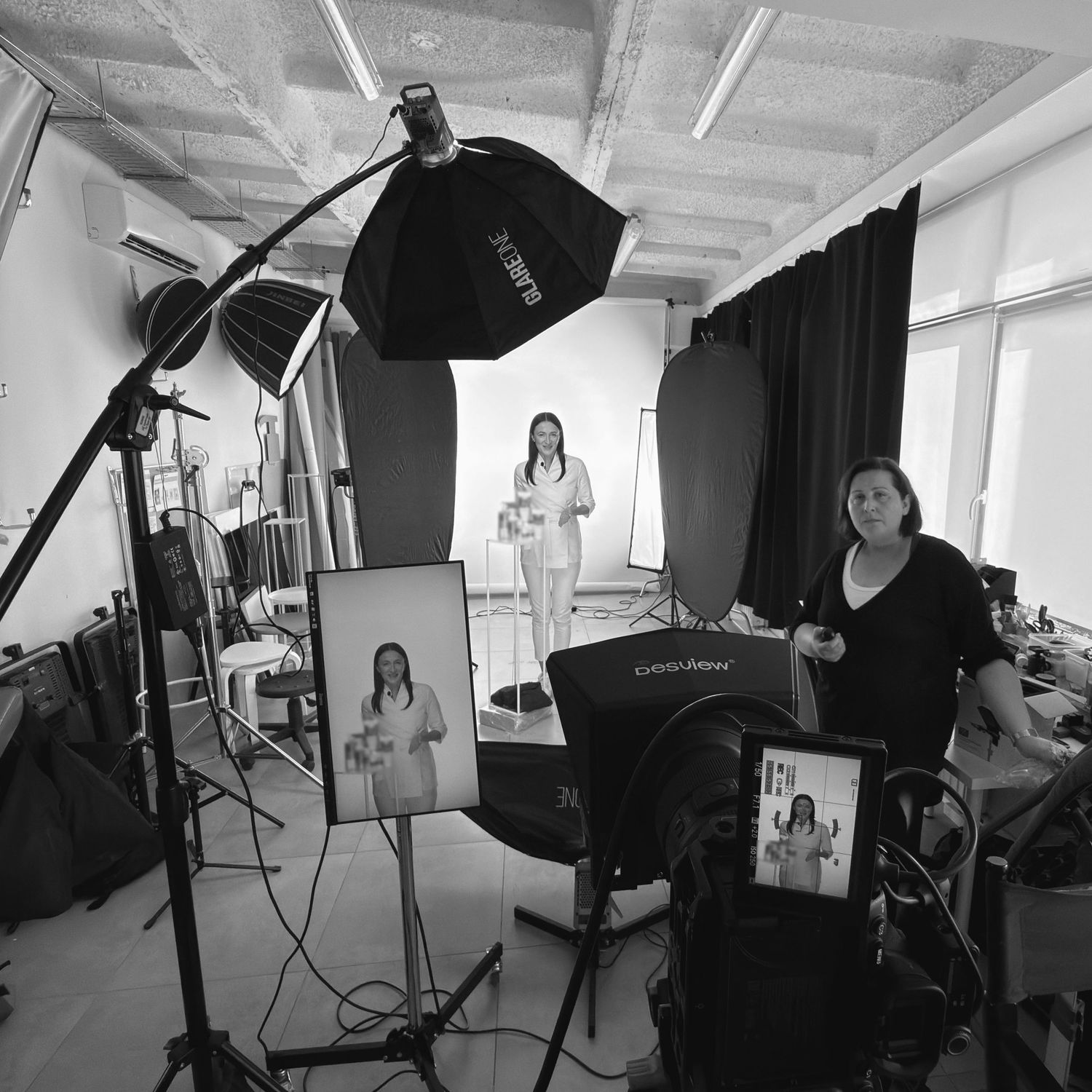 Czarno-białe zdjęcie profesjonalnego studia fotograficznego z oświetleniem oraz modelem podczas sesji zdjęciowej.