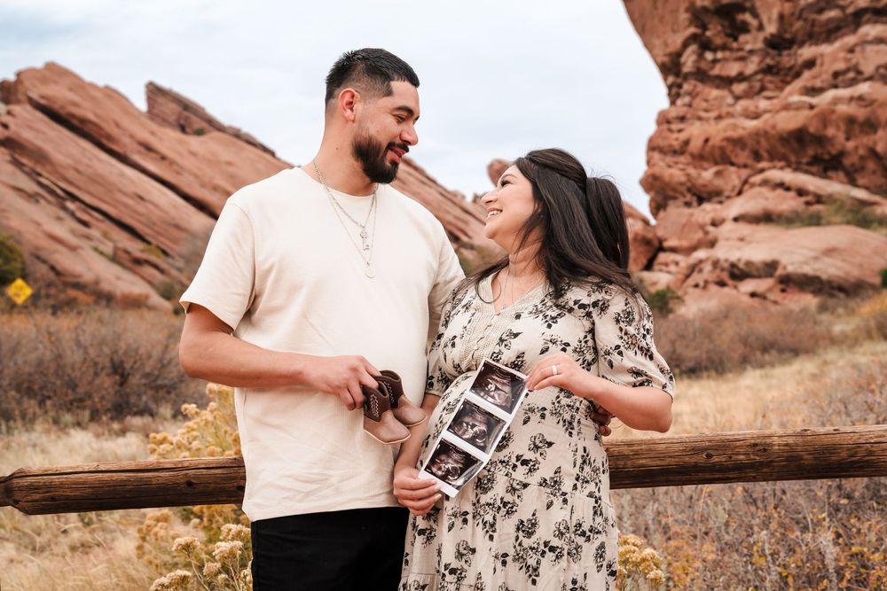 Couple holding ultrasound photos at Red Rocks Park, Colorado, sharing a joyful pregnancy announcement moment.
