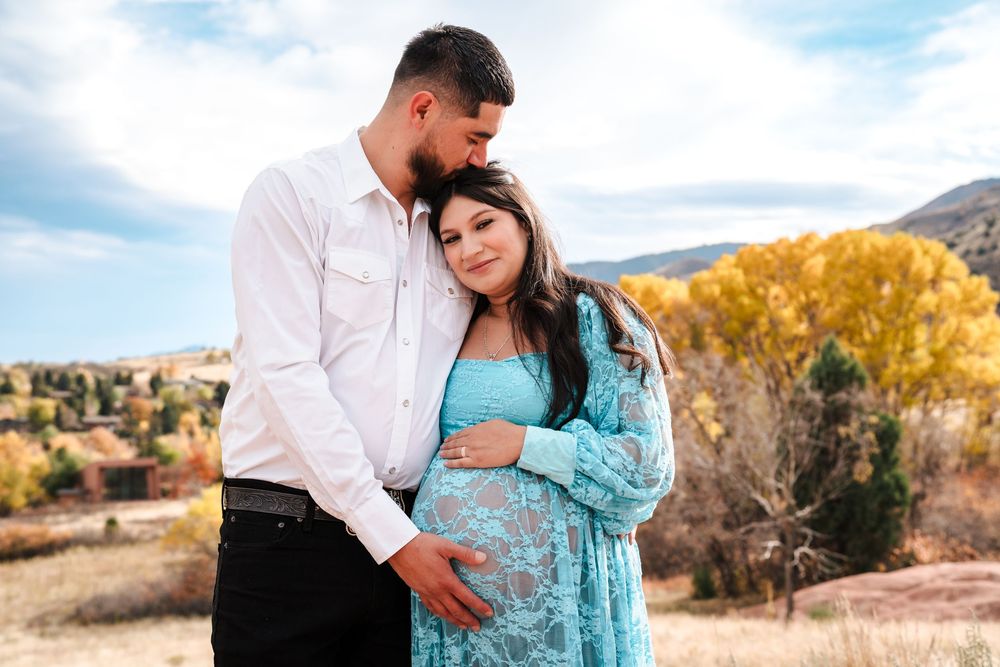 Couple sharing a tender maternity photo outdoors with fall foliage and mountains in the background.