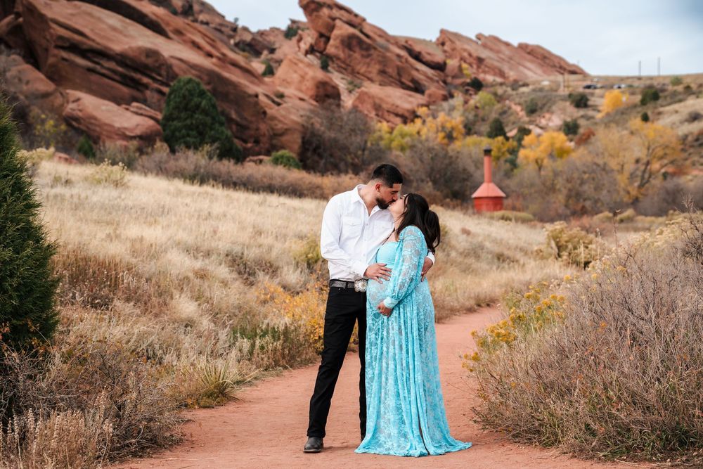 Couple kissing in turquoise dress at Red Rocks Park, Colorado, surrounded by red rock formations and golden autumn grass.