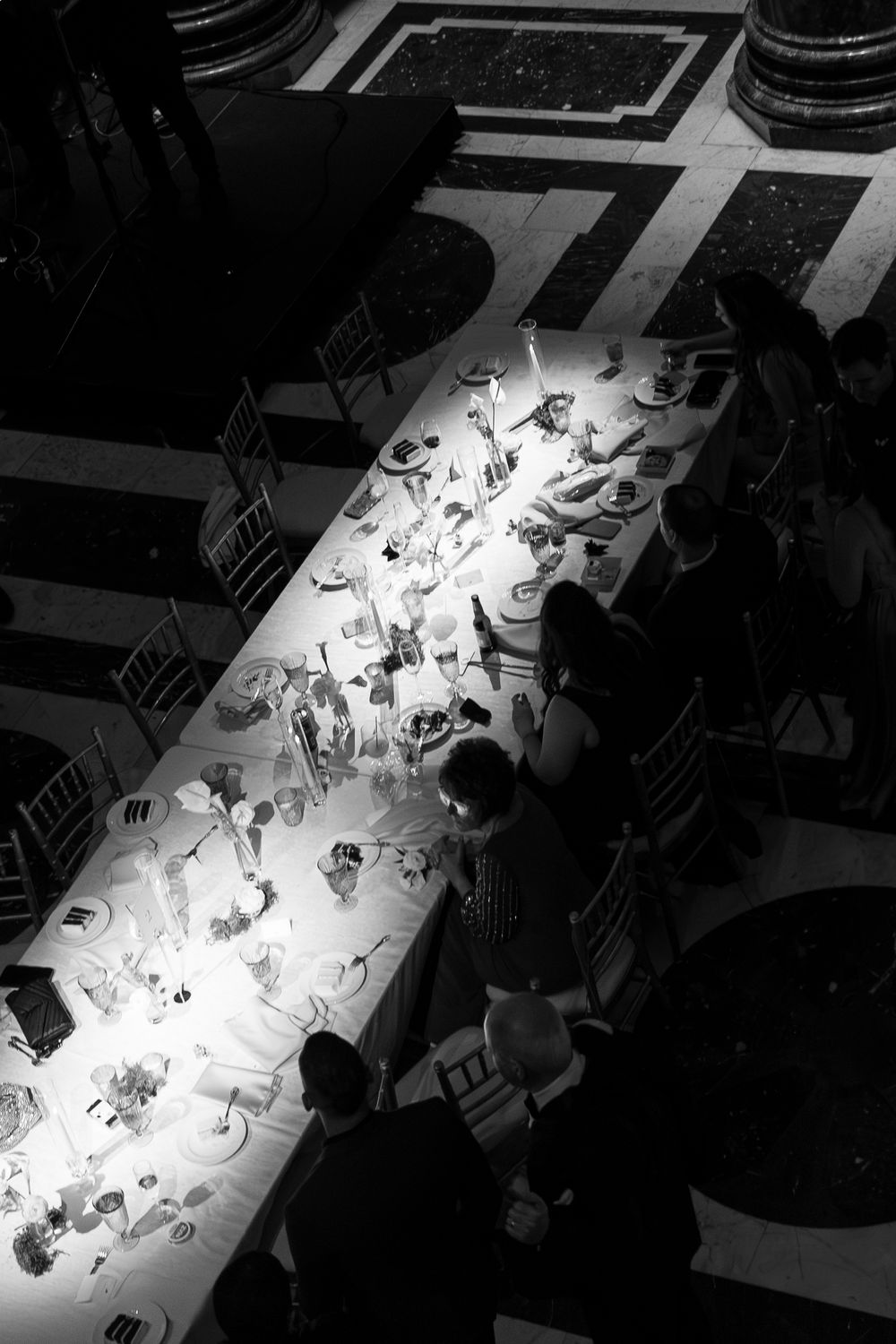 Aerial black and white photo of elegantly set banquet table with candles and guests dining at formal event.