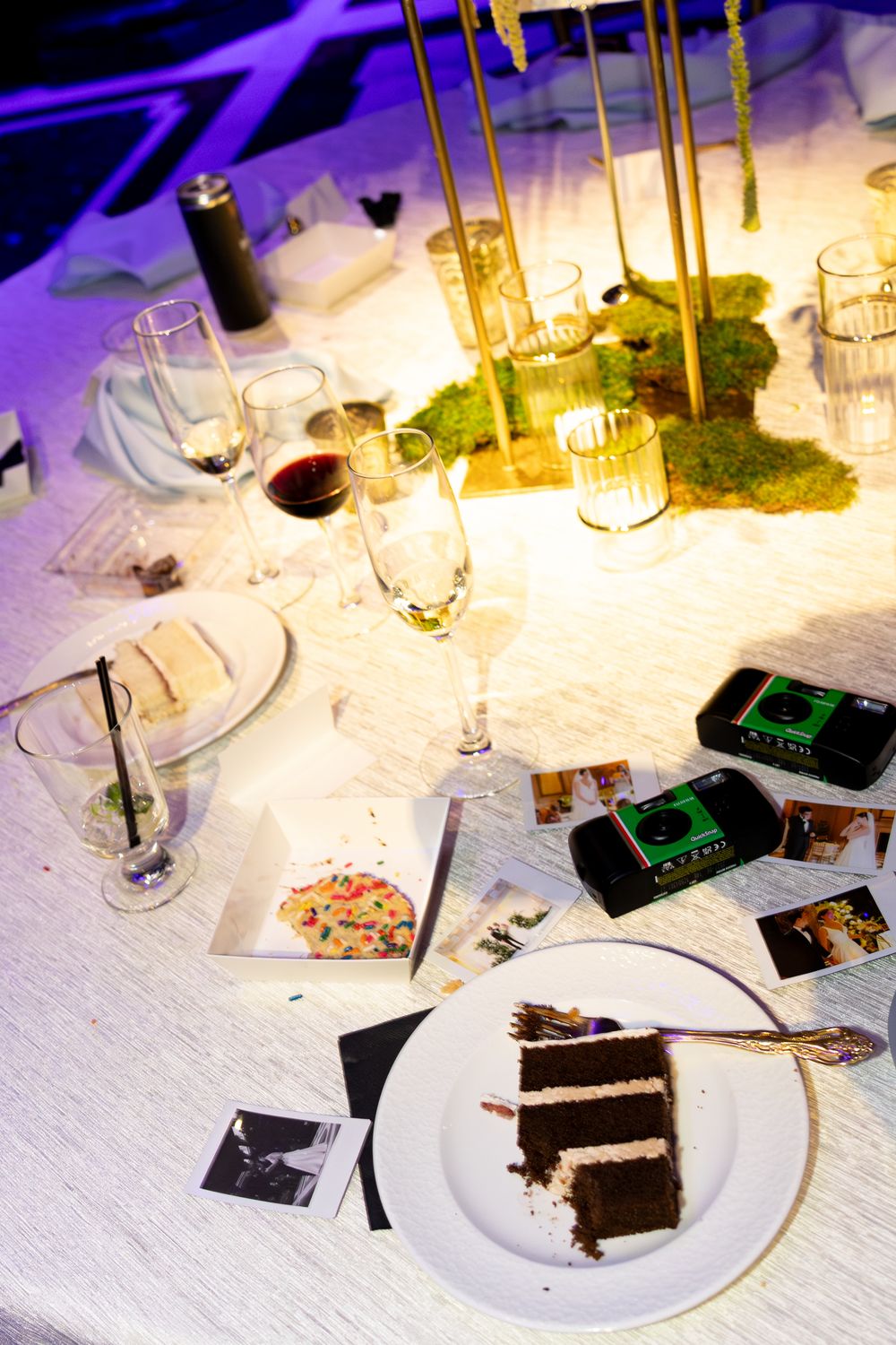 Elegant wedding reception table with chocolate cake, champagne flutes, wine glasses, gold candelabras, and moss centerpiece.