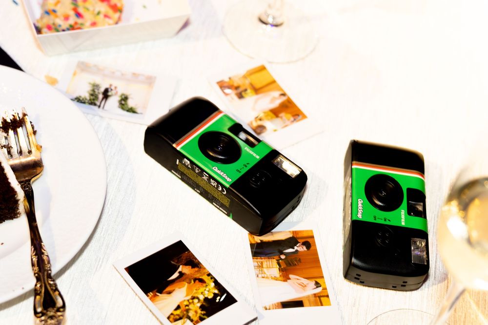 Disposable cameras and Polaroid photos scattered on a white tablecloth at a wedding reception.