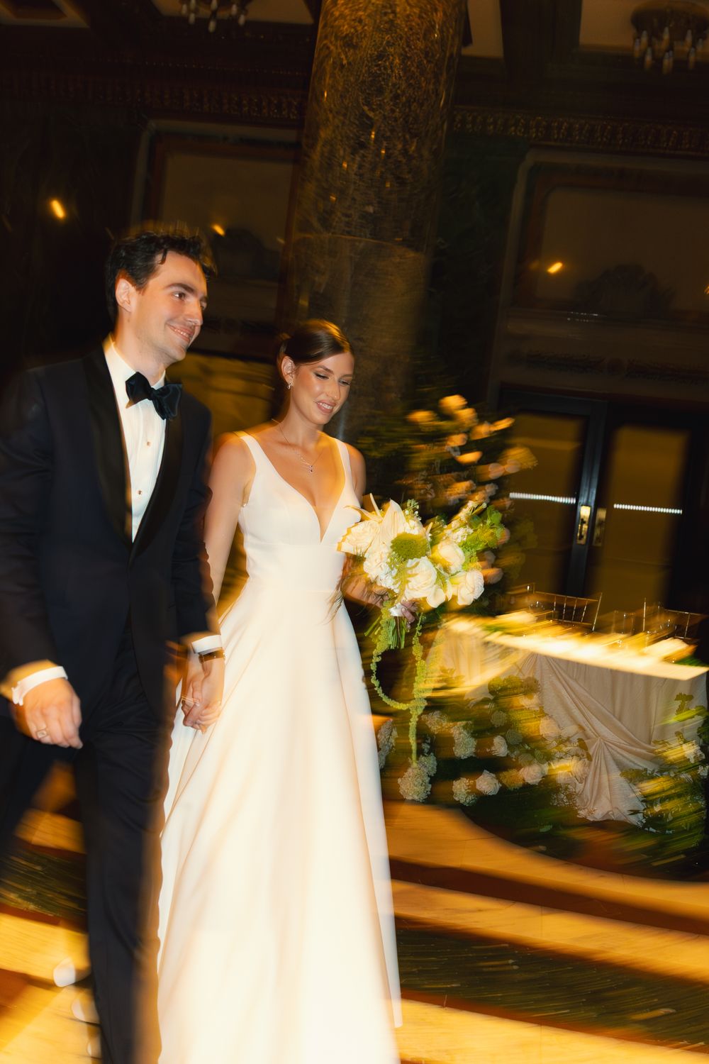 Bride and groom walking together at wedding reception, bride holding white bouquet in classic gown.
