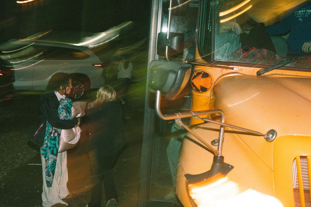 Person embracing near a yellow school bus door at night with motion blur lighting.
