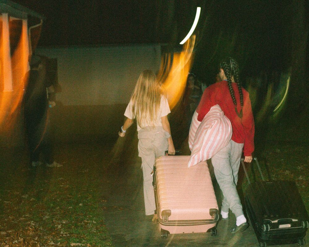 Two women pulling pink luggage through a dark outdoor path at night.