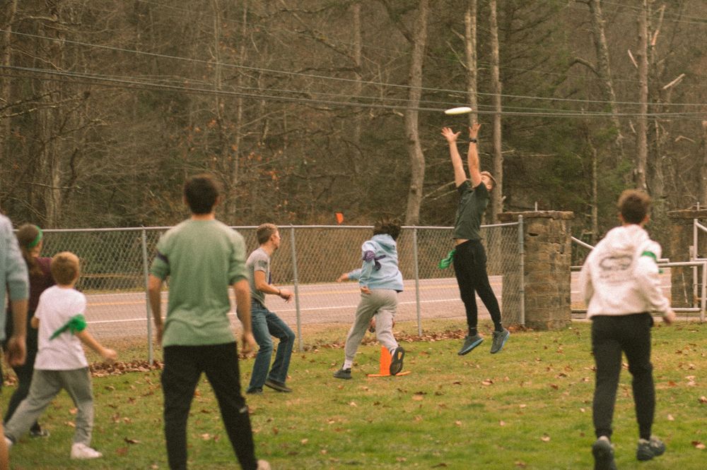 Group of teens playing ultimate frisbee outdoors near a fence in autumn.
