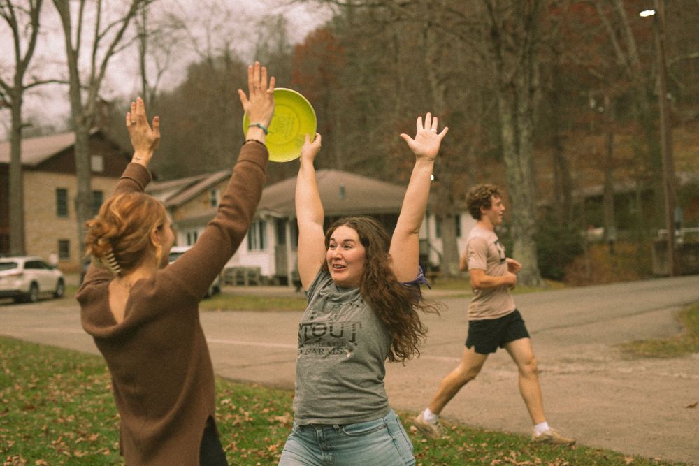 Two women celebrating with hands raised near a yellow frisbee outdoors in a residential area.