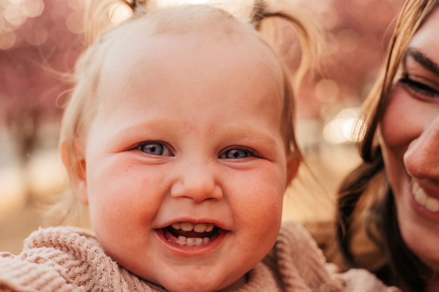 Smiling baby with blue eyes and rosy cheeks held by mom  with soft background |  How to Get Nice Family Photos with a Wild Toddler