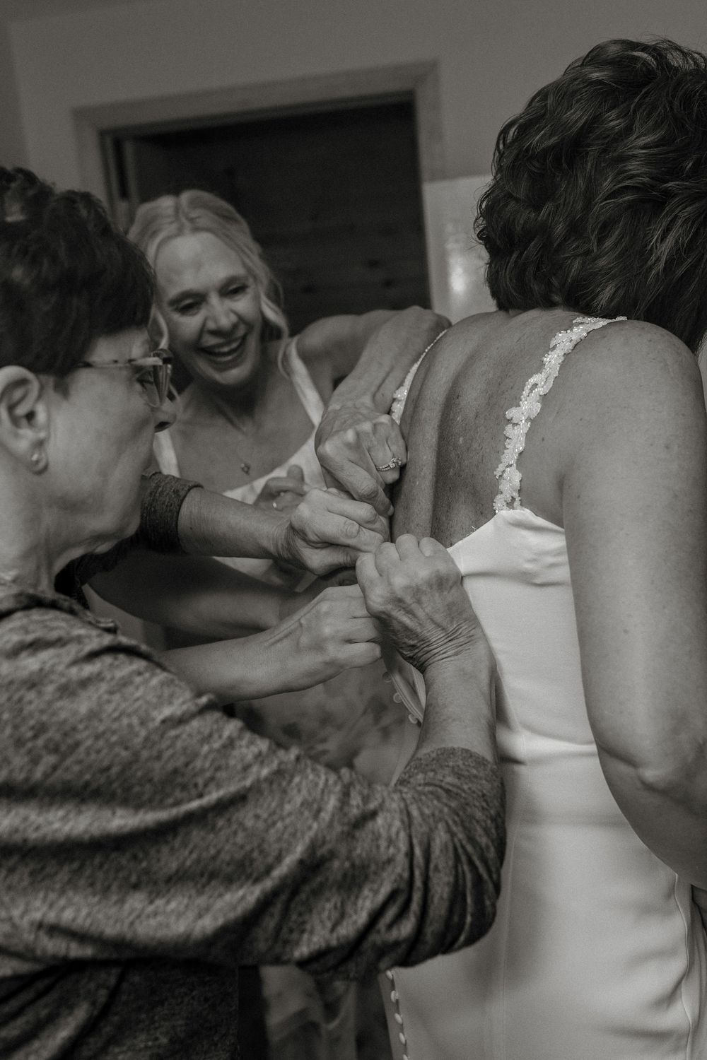 Black and white photo of women helping a bride button her wedding dress before the ceremony.