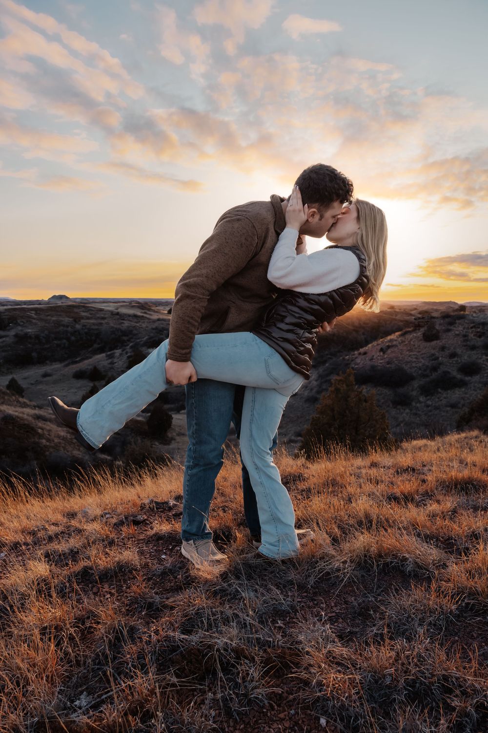 Couple sharing a romantic kiss at sunset on a grassy hillside, man dipping woman in a loving embrace. Bismarck, ND photographer