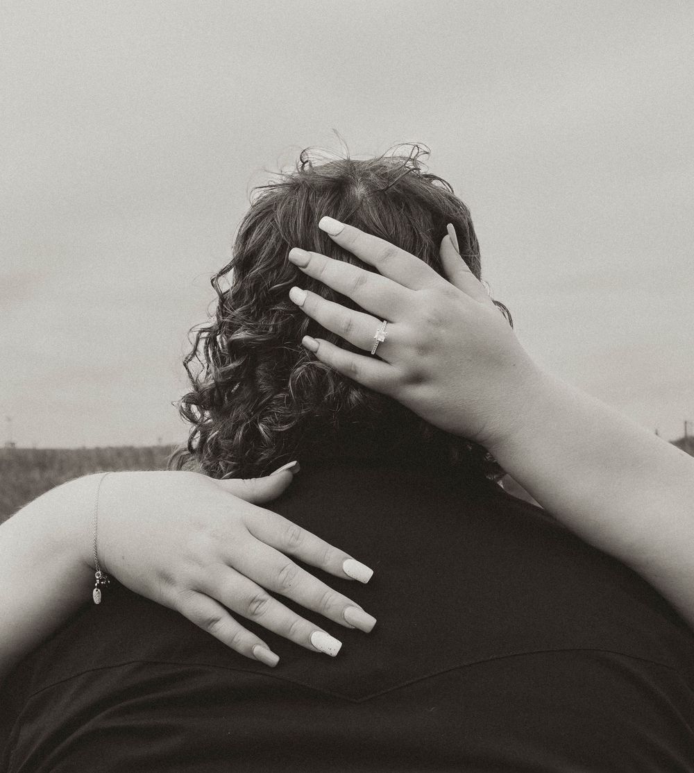 Black and white photo of a couple embracing, woman with curly hair and manicured nails resting hands on partner's back. Bismarck, ND photo