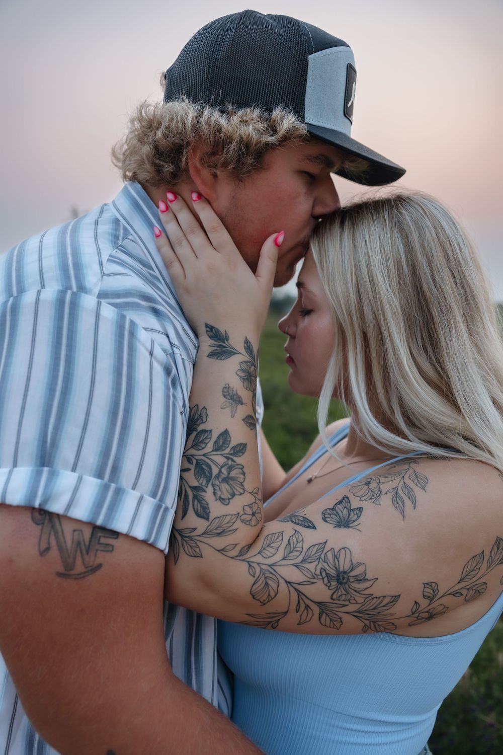 Couple with tattoos sharing a romantic moment at sunset, woman in blue top holding man's face tenderly. Garrison, ND Photographer