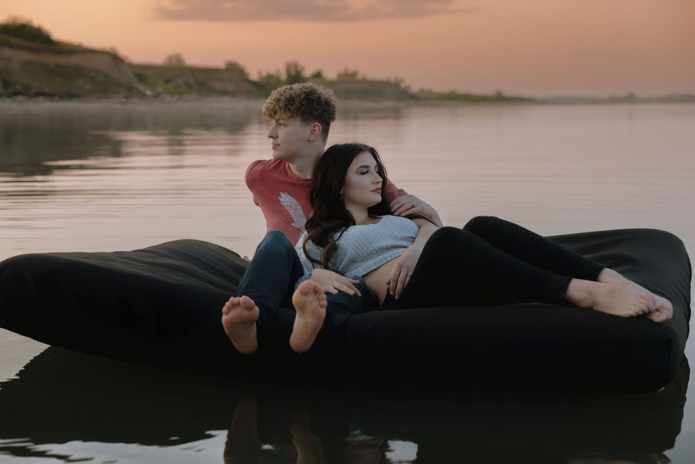 Couple relaxing on a black inflatable lounger floating on calm water at sunset. Garrison, ND Photographer