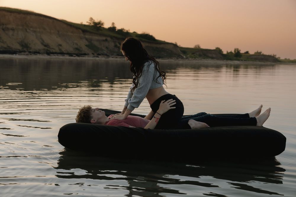 Romantic couple on inflatable raft floating on calm water at sunset, woman sitting over man. Garrison, ND Photographer