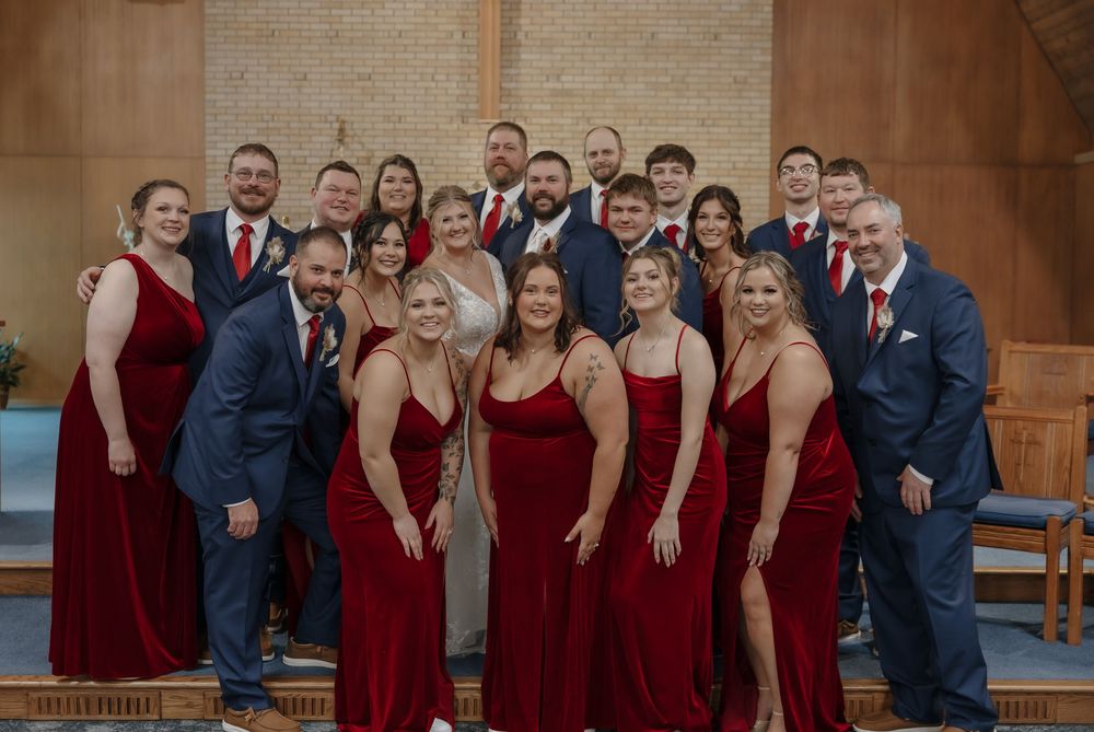 Wedding party in red dresses and navy suits posing together inside a church. Garrison, ND Photographer