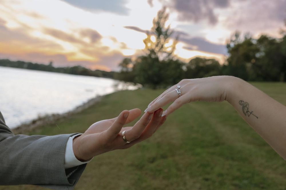 Close-up of couple holding hands at sunset revealing diamond engagement ring near lakeside venue. Bismarck, ND travel photographer