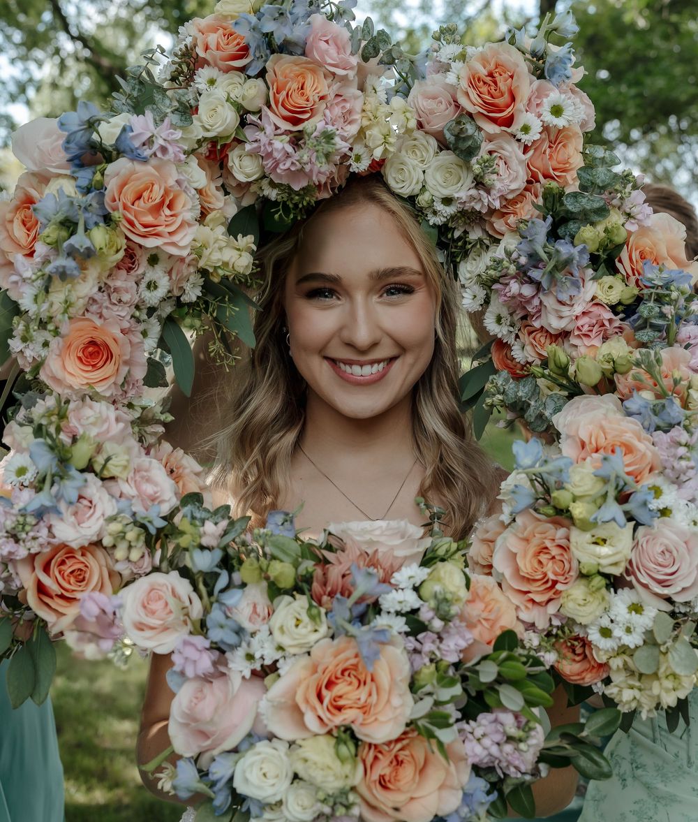 Smiling bride framed by a large circular wreath of peach roses and pastel wildflowers outdoors. Hankinson, ND photographer