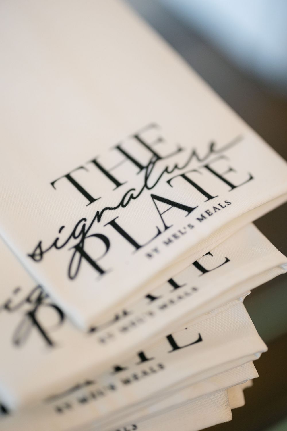 Stack of white programs for The Signature Plate by Mel's Meals dining event.