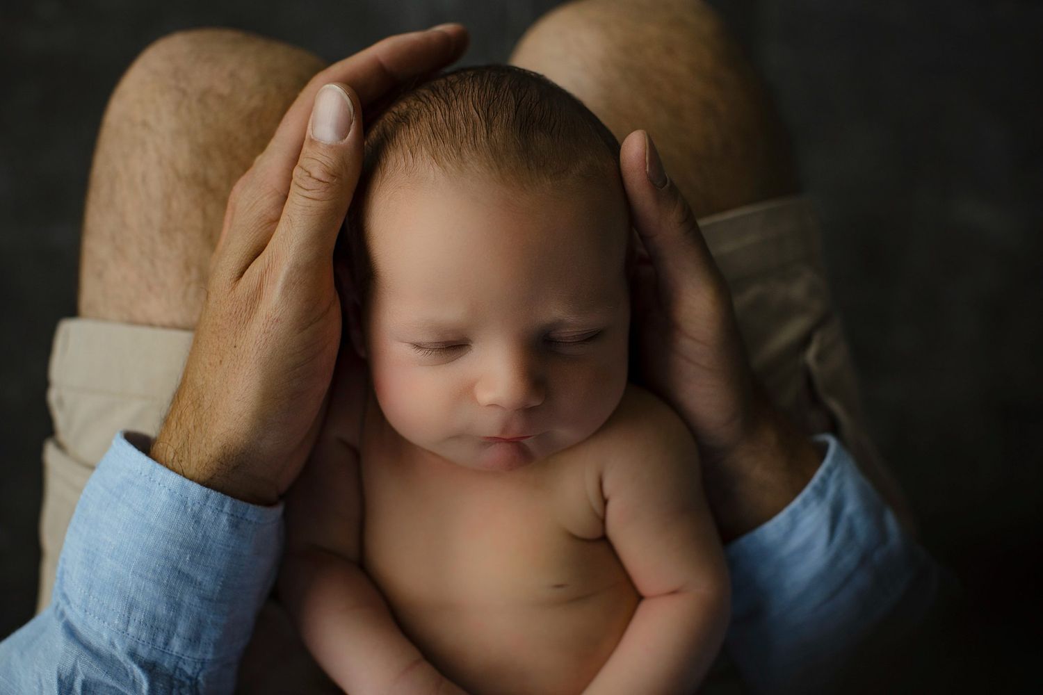 Newborn baby sleeping peacefully cradled in parent's gentle hands during a professional newborn photography session.