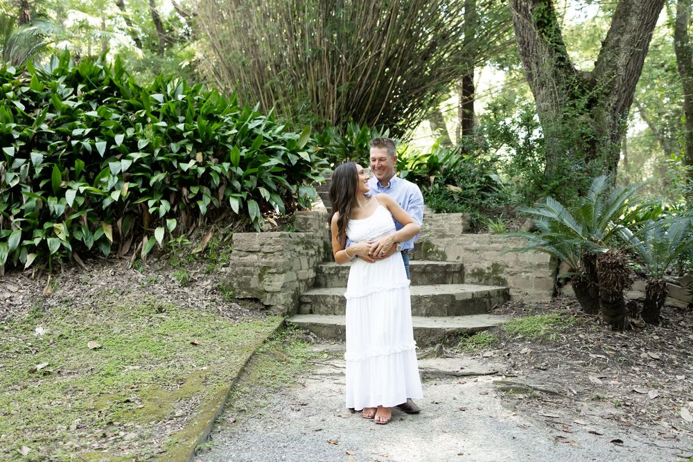 Couple embracing and kissing on a garden path surrounded by lush tropical greenery and stone steps.