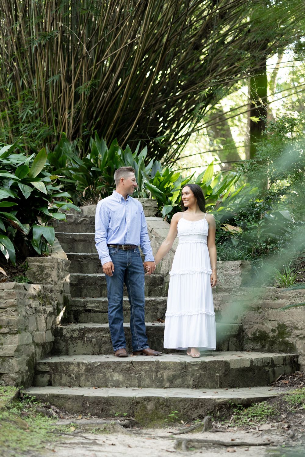 Couple holding hands on stone steps surrounded by lush tropical greenery.
