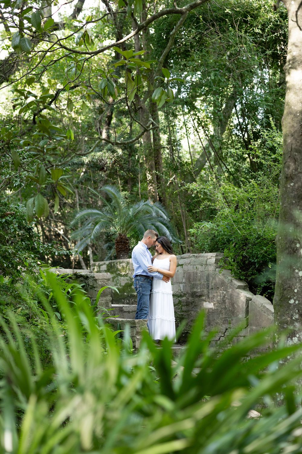 Romantic couple embracing on stone steps surrounded by lush tropical greenery in a beautiful garden setting.