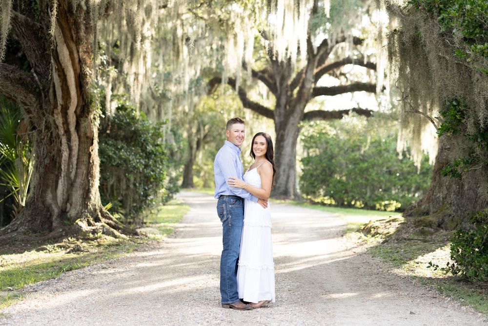 Couple posing on a scenic tree-lined path draped with Spanish moss during an outdoor engagement session.