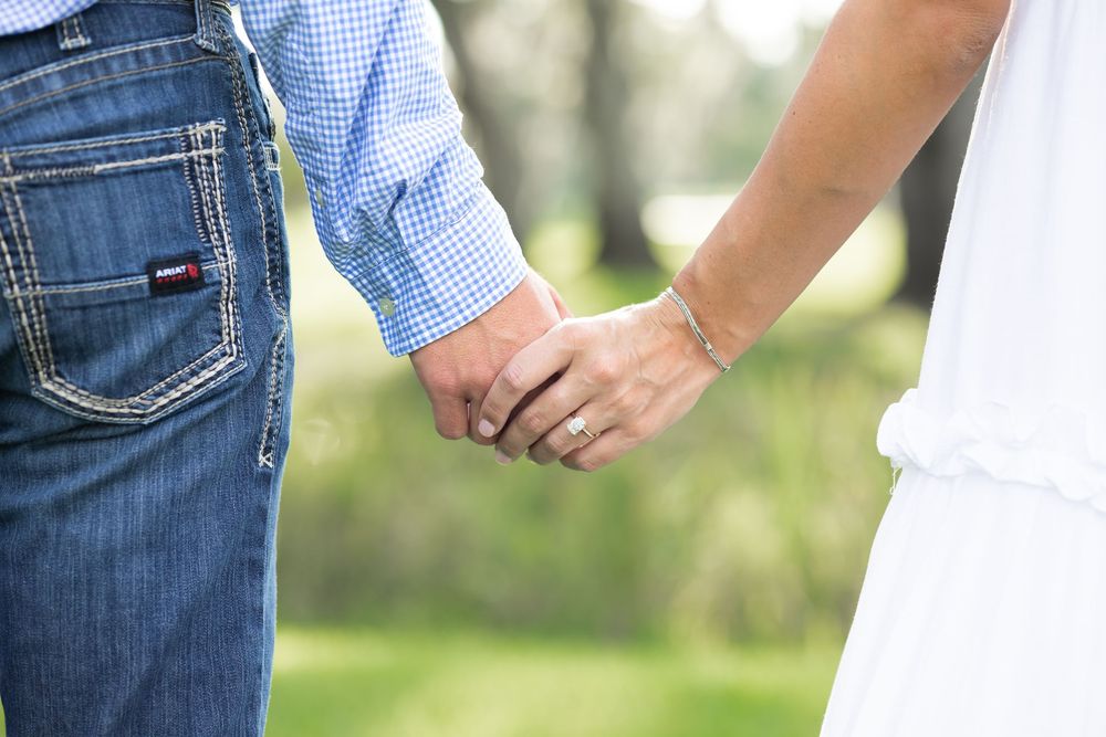 Close-up of engaged couple holding hands showing diamond ring and bracelet outdoors.