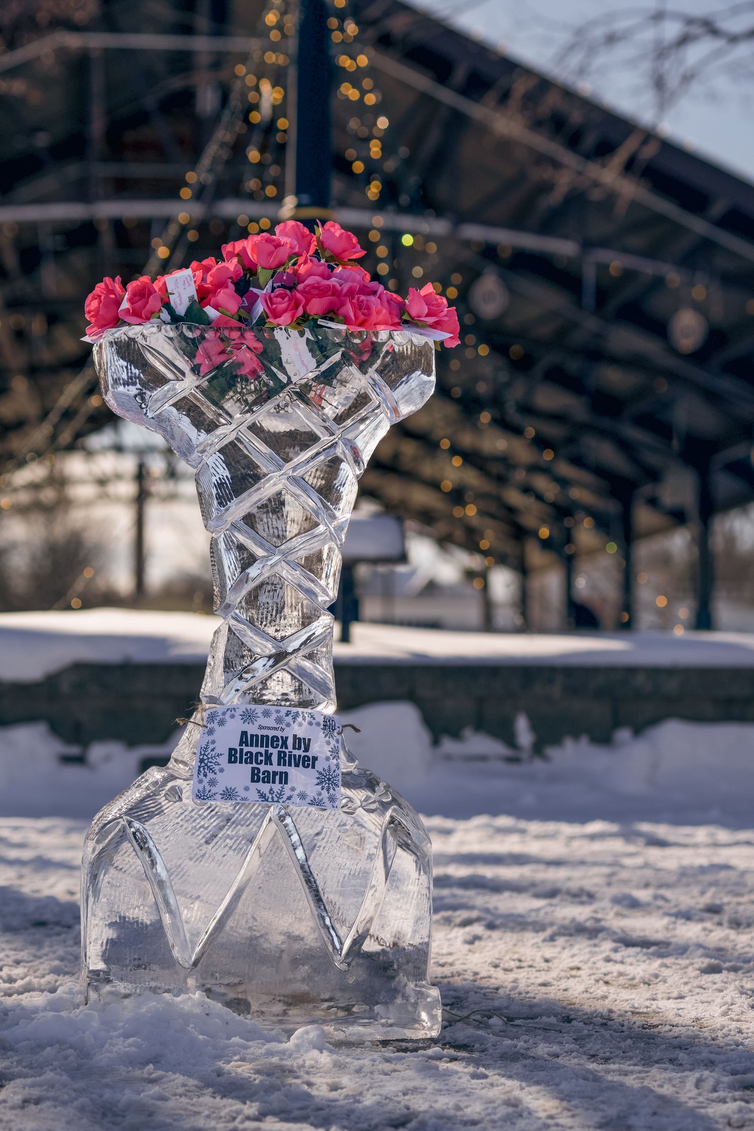 Ice sculpture vase with pink roses displayed outdoors in winter snow, created by Black River Barn.