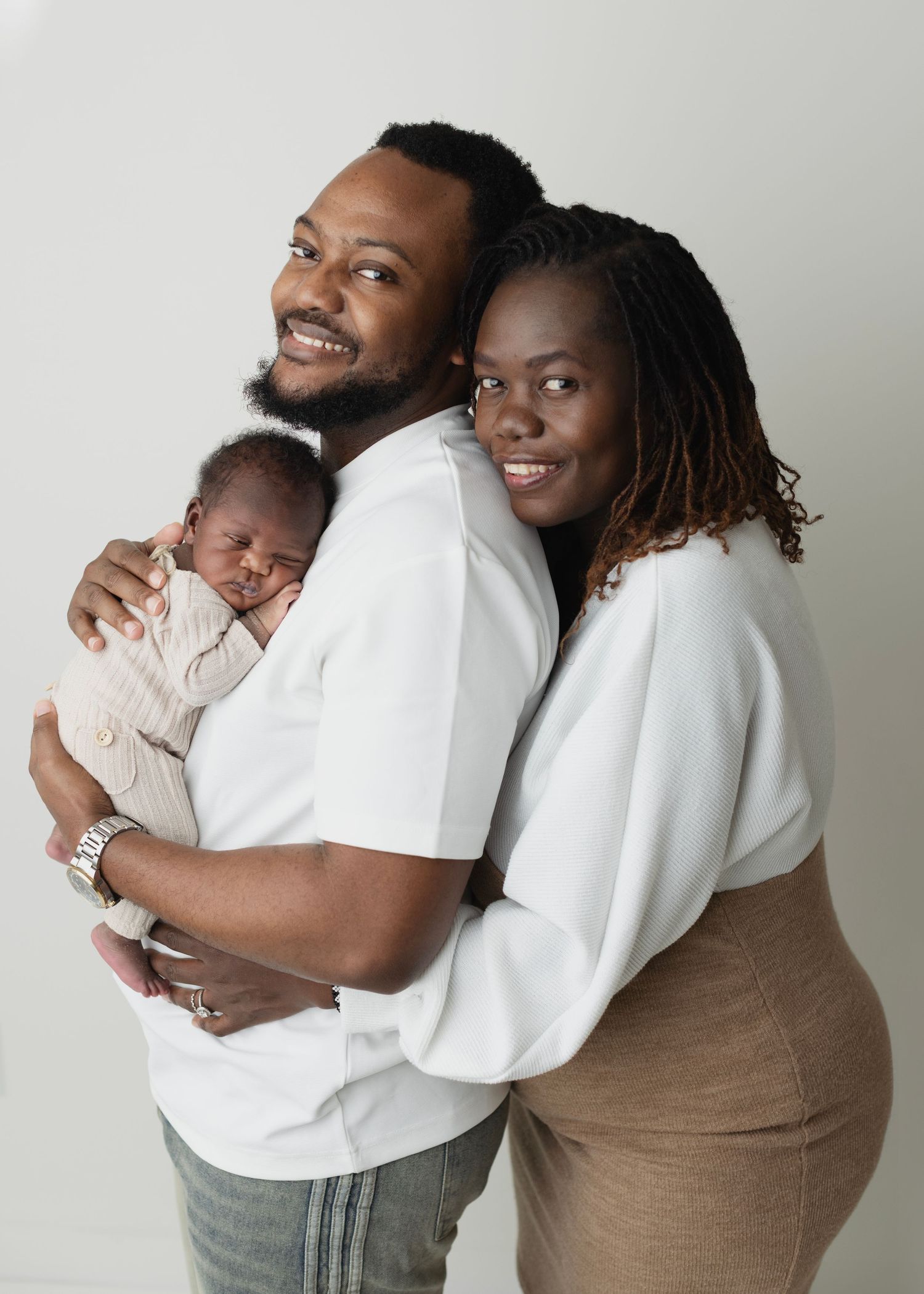 Happy couple smiling and holding their newborn baby in a professional studio portrait photo. Elizabeth Lang Photography Surrey