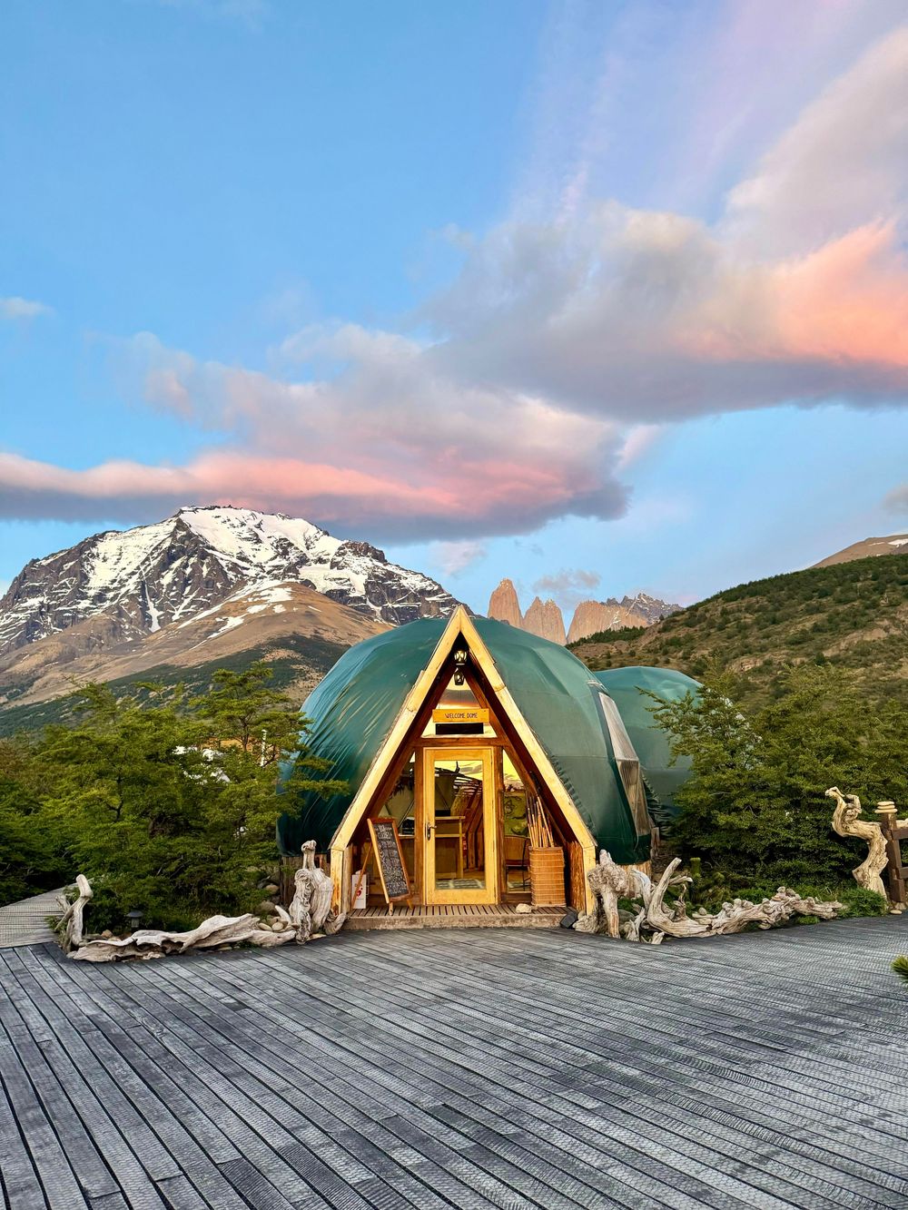 Luxury glamping dome on wooden deck at sunset with snow-capped Patagonian mountains in the background.