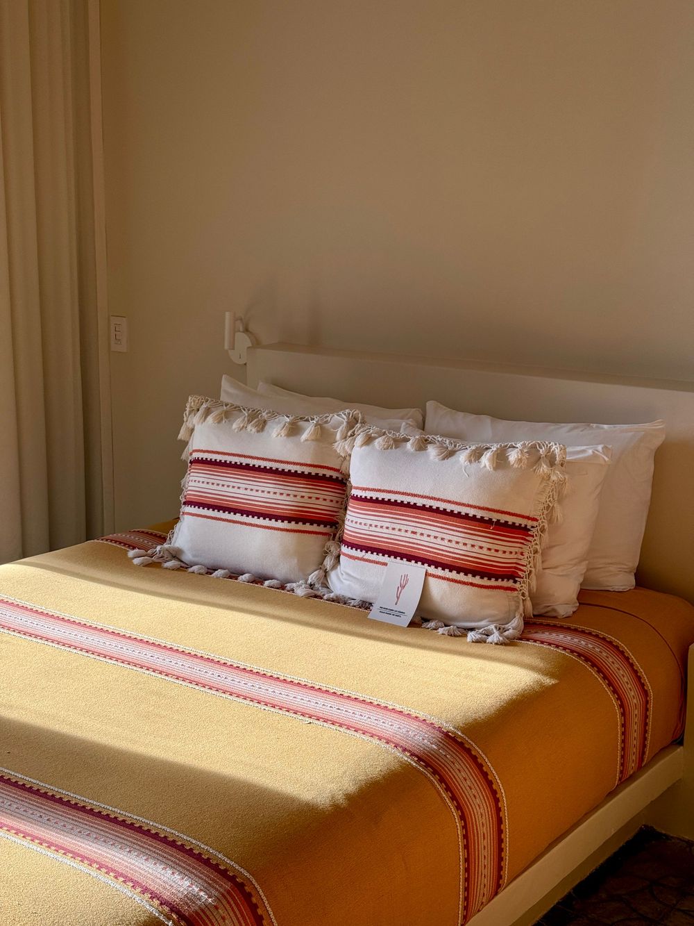 Cozy bed with yellow striped blanket, decorative red and white tassel pillows, and white fringe accent pillows.