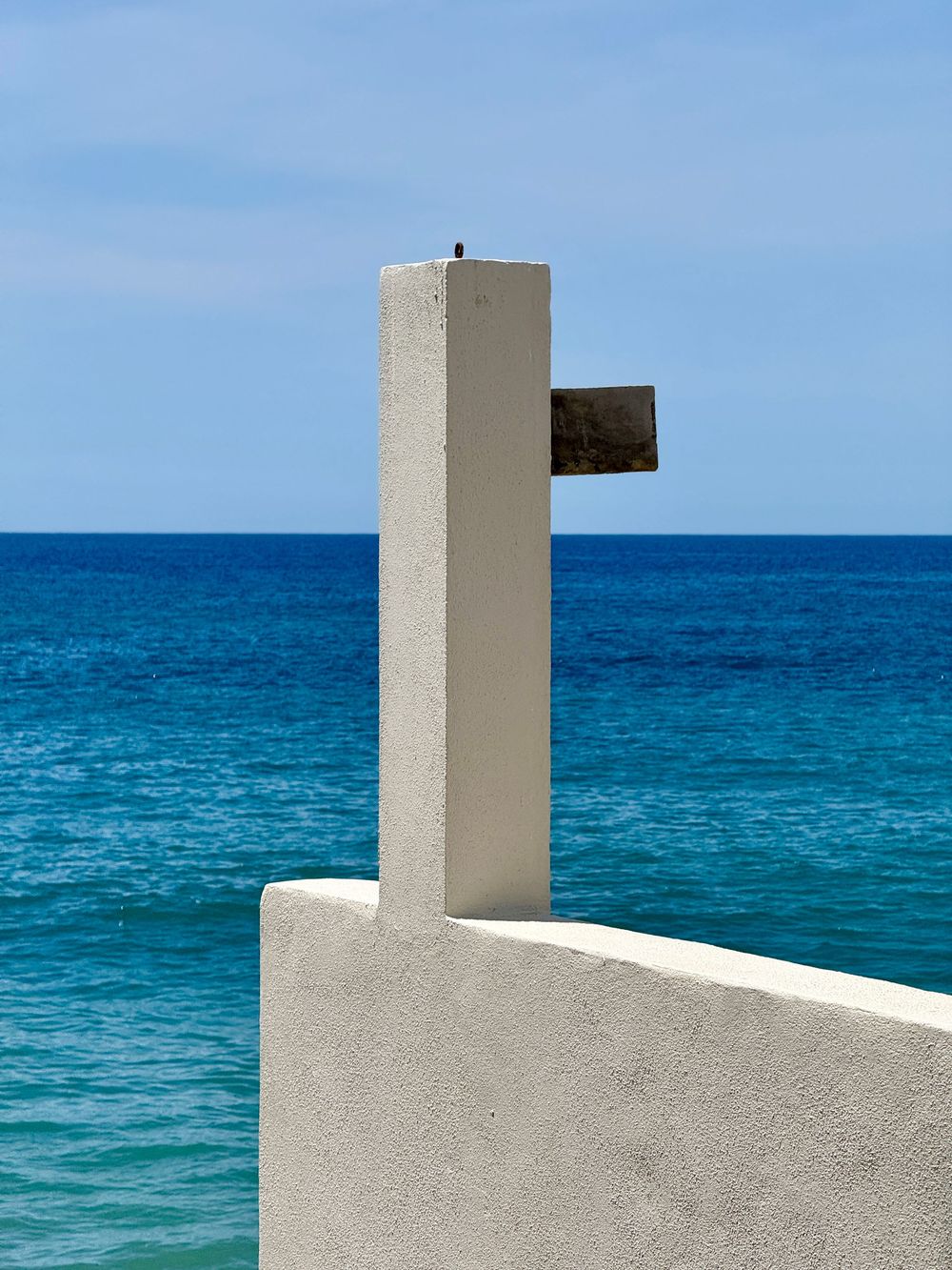 White concrete outdoor shower structure against a vivid turquoise ocean and blue sky backdrop.