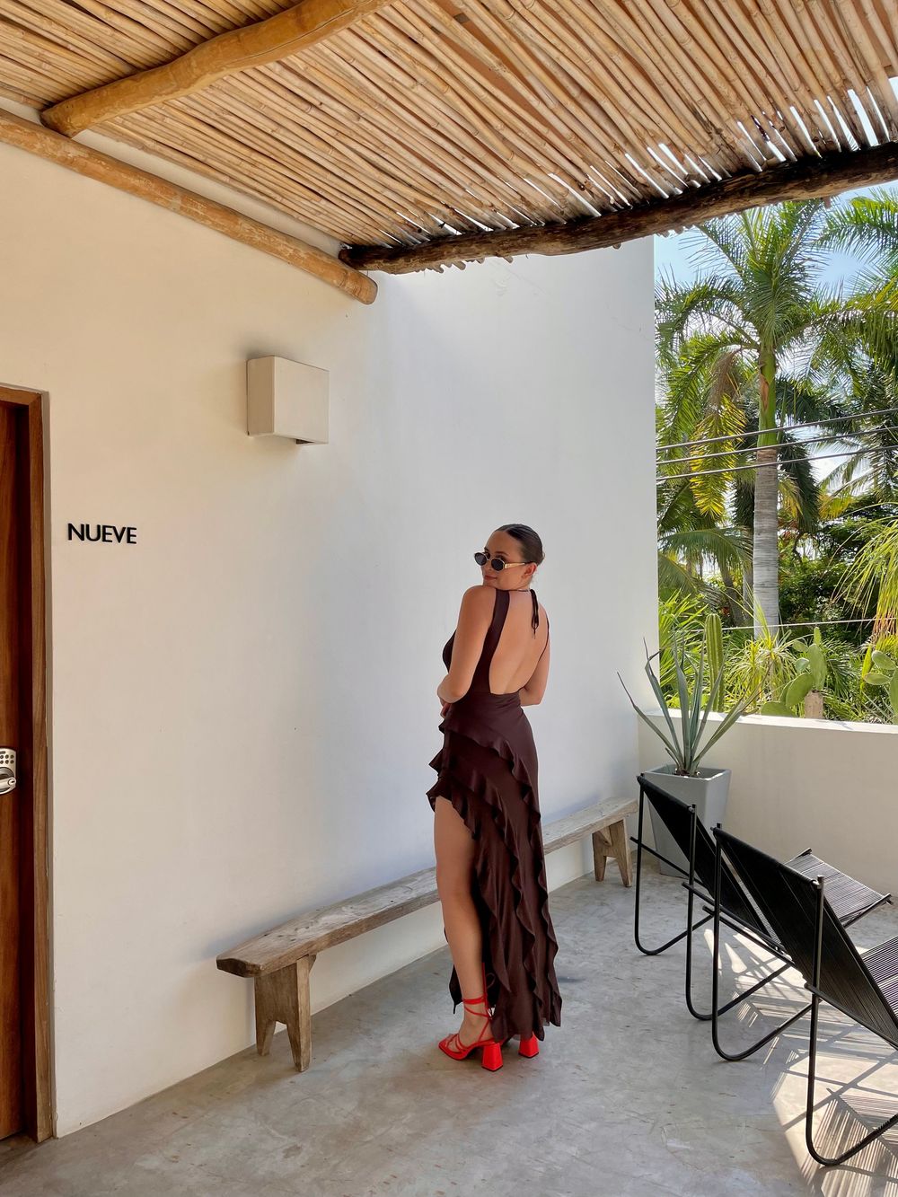 Woman in backless brown ruffled dress with red heels standing on a terrace at boutique hotel Bonito in Sayulita with tropical palm trees.