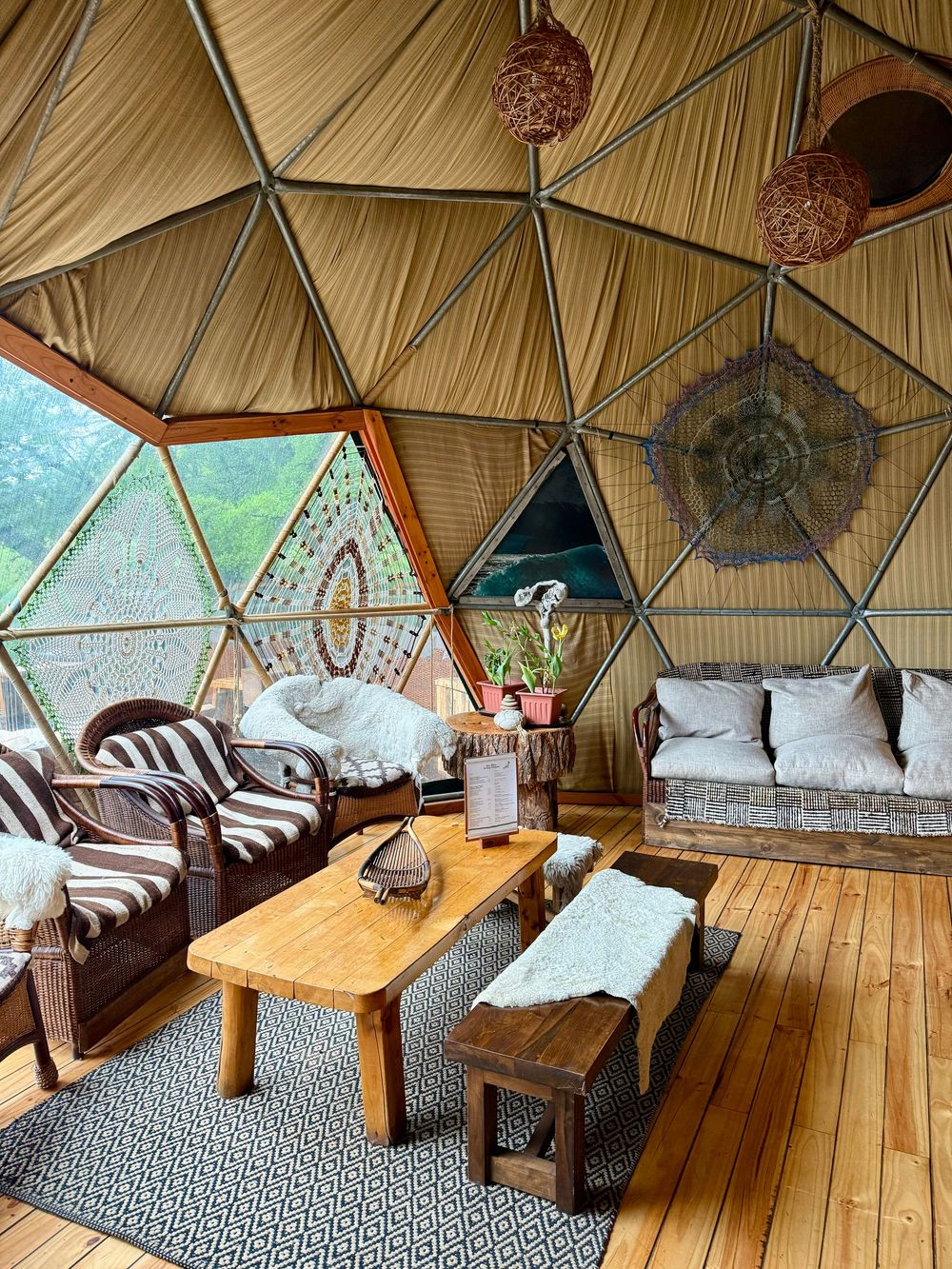 Cozy geodesic dome interior with wooden floors, eclectic furniture, and woven pendant lights.