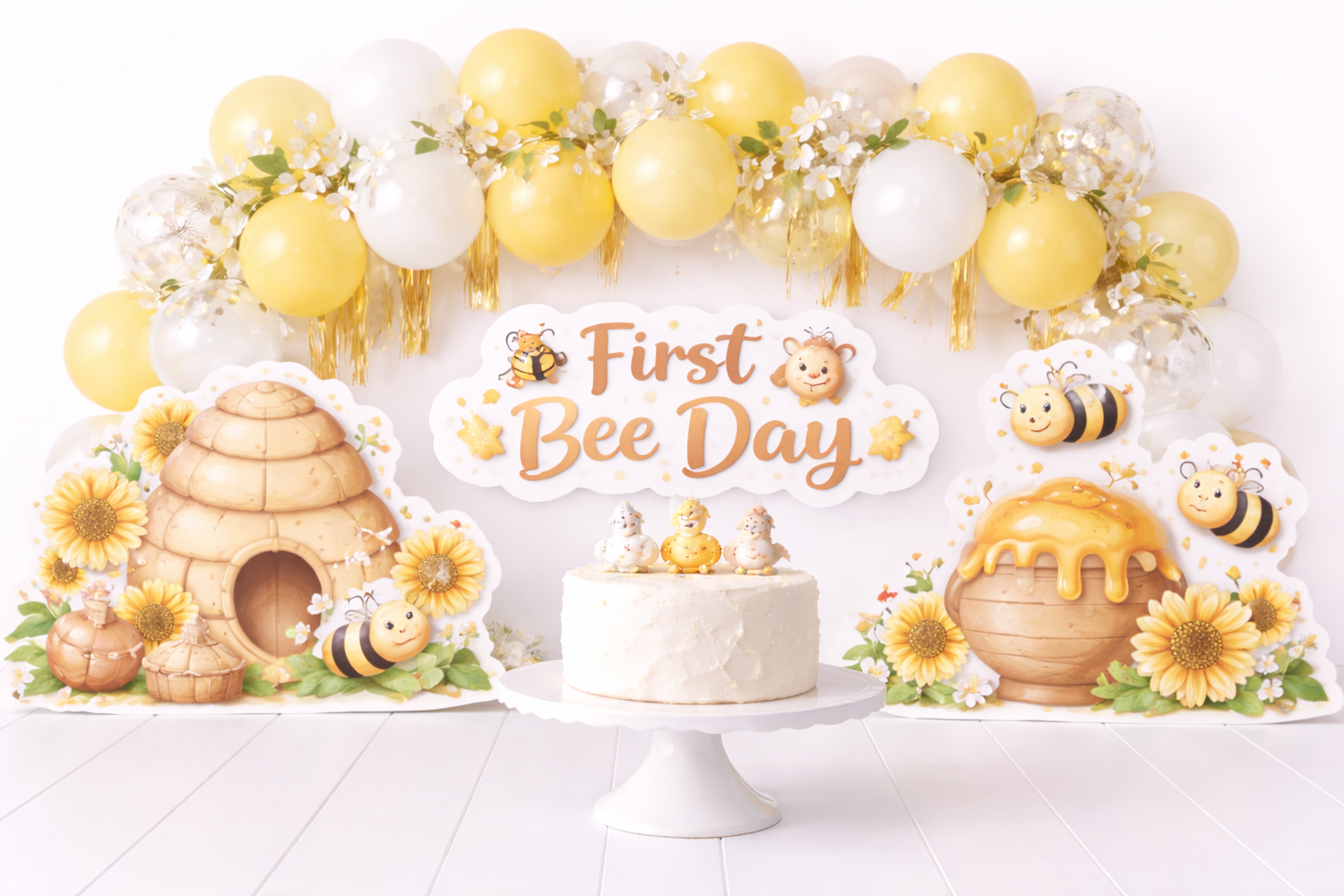 First Bee Day birthday setup with white cake, beehive decor, sunflowers, cute bees, and yellow balloon garland backdrop.Elizabeth Lang