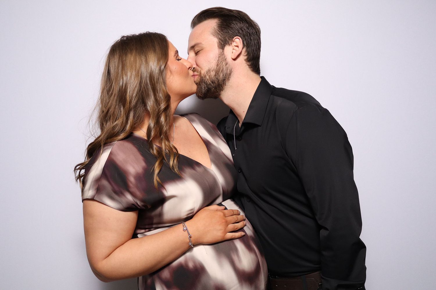 Pregnant couple sharing a tender kiss against a white background, celebrating their upcoming arrival.