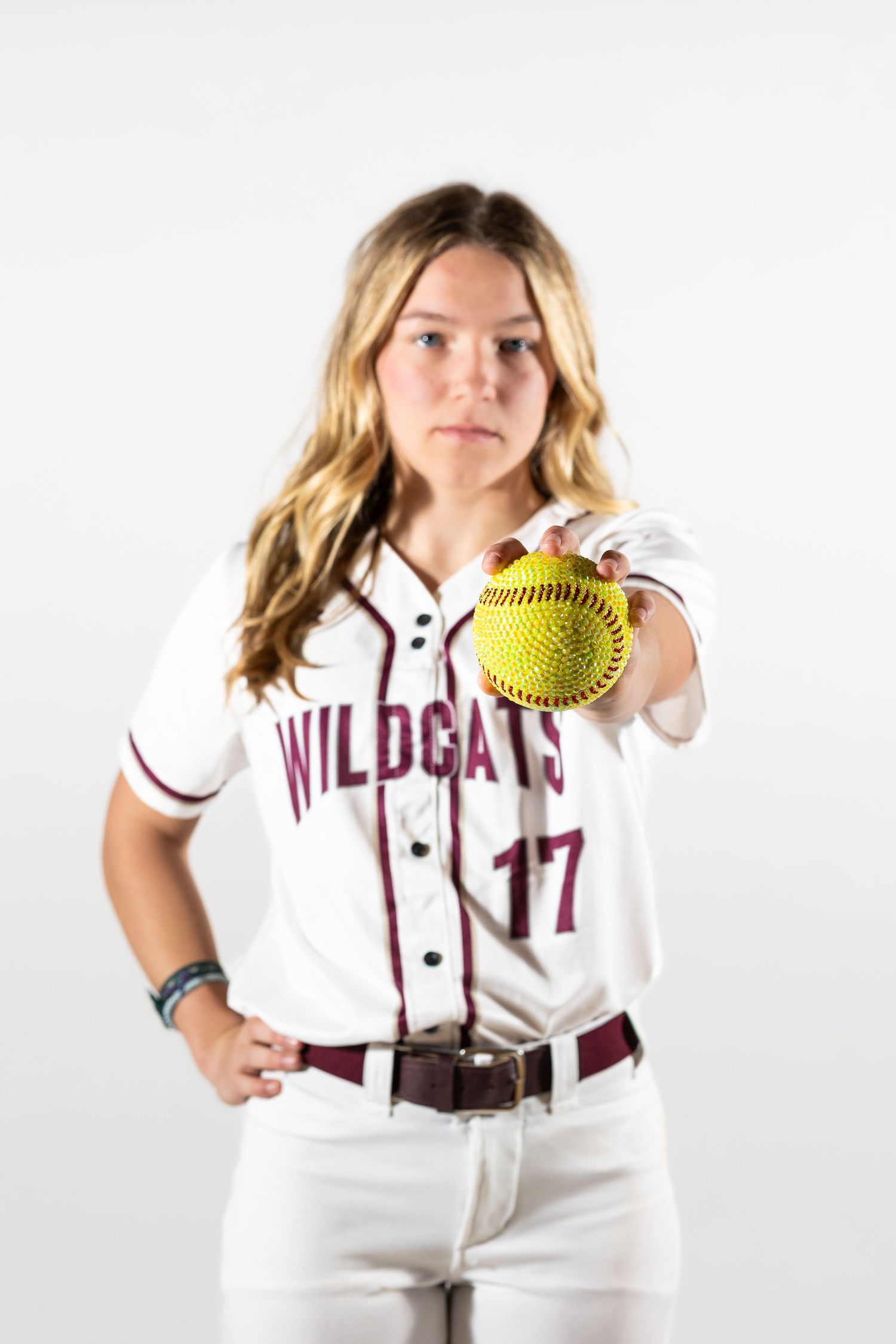 Female softball player in Wildcats #17 jersey holds yellow softball toward camera in professional sports portrait.