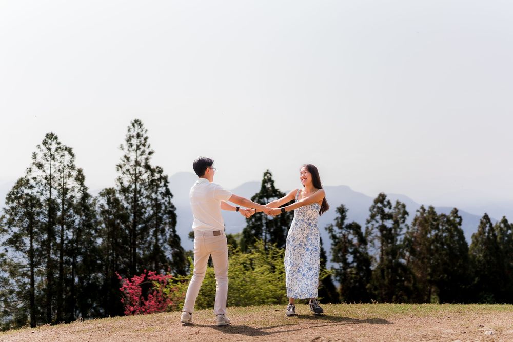 Couple holding hands and dancing together on a hilltop surrounded by tall trees and misty mountains.
