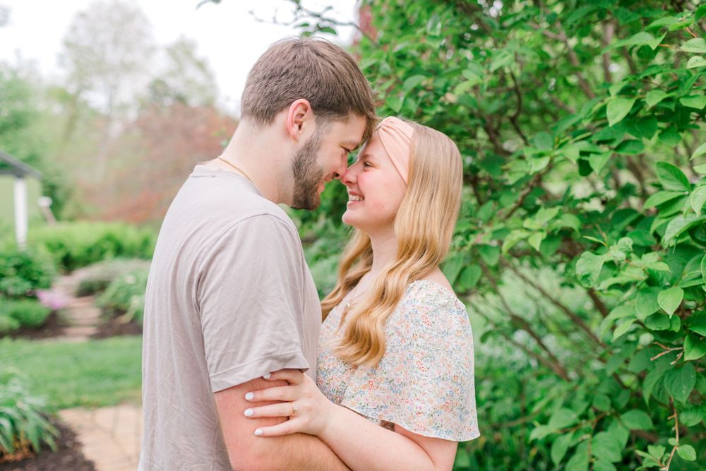 Couple sharing a romantic moment outdoors, smiling at each other near lush green garden foliage.