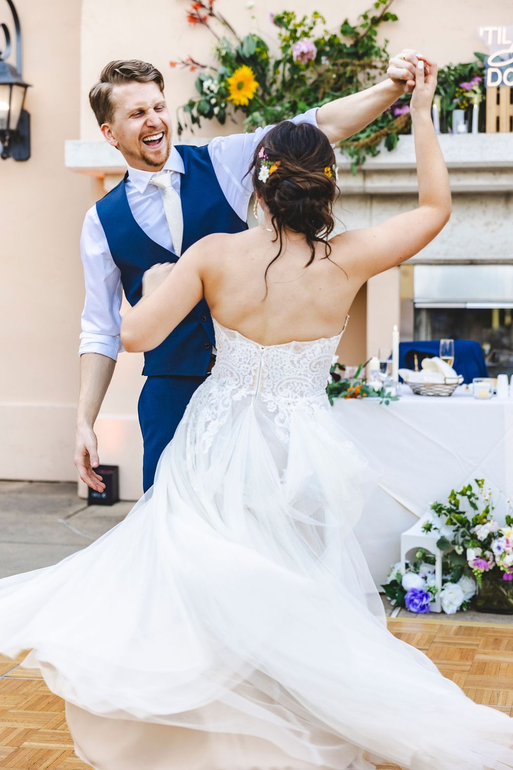 Bride and groom share joyful first dance outdoors, groom smiling as he twirls bride in elegant white gown.