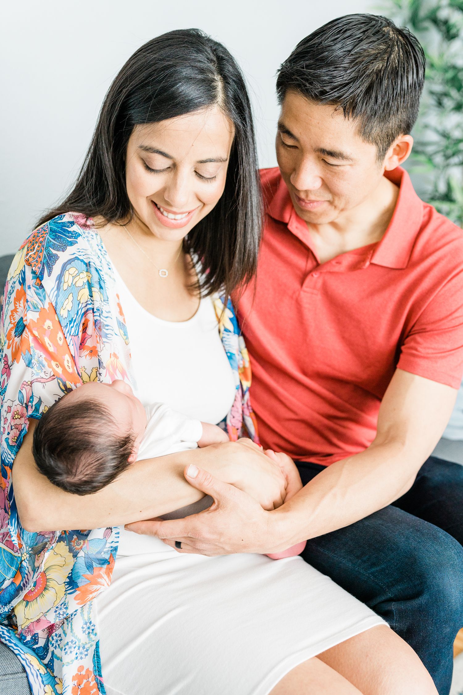 Happy Asian couple sitting together smiling while cradling their newborn baby.