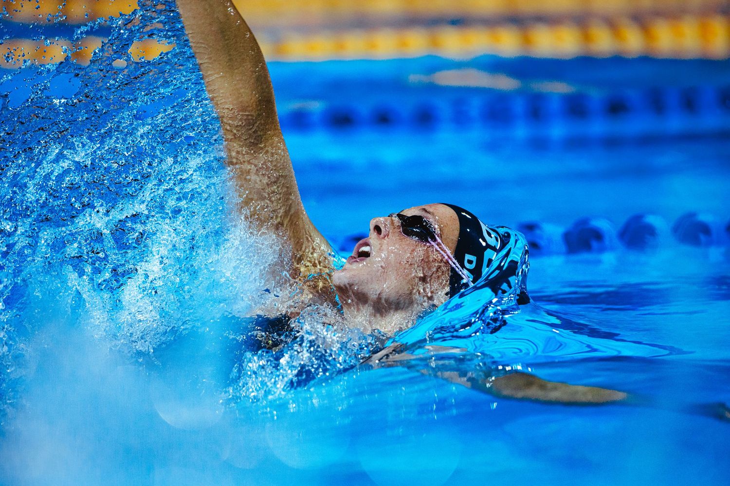 Competitive swimmer performing butterfly stroke in a professional pool with colorful lane dividers during a championship event.