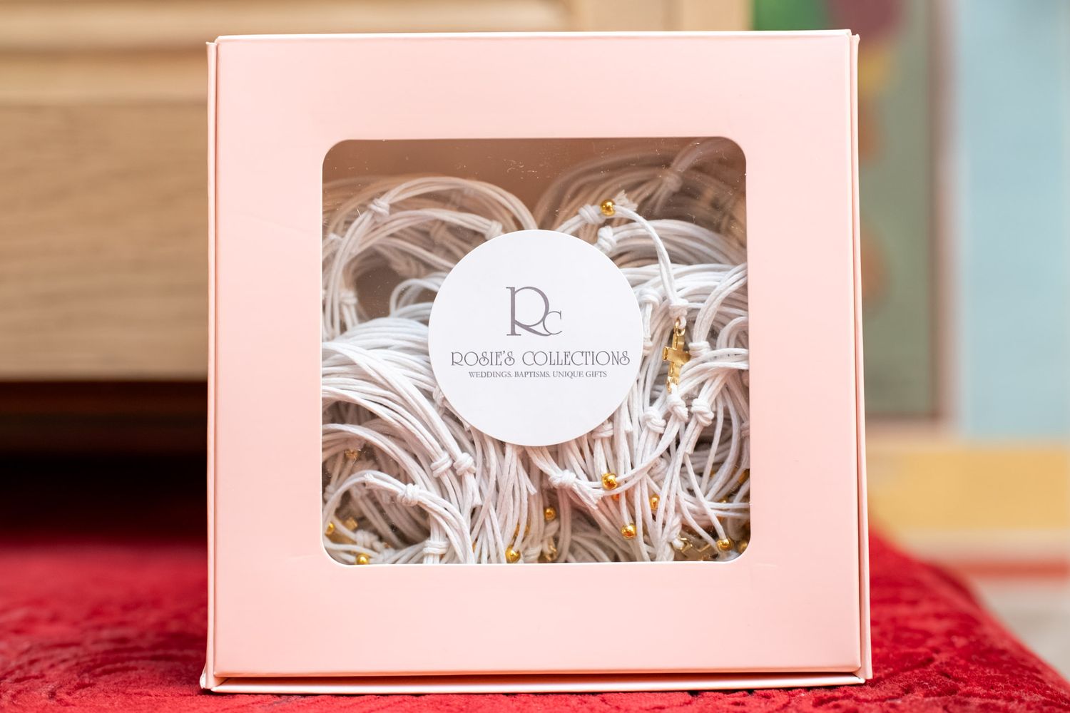 A pink gift box with a clear window displaying white hair ties from Romer Collections brand.