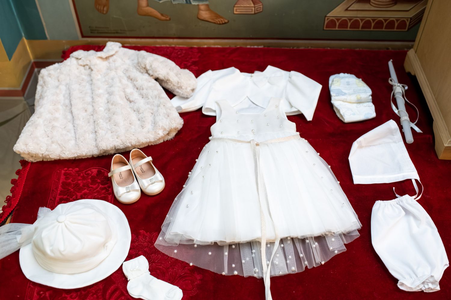 A complete white baptism outfit including dress, coat, shoes, hat, and accessories on red velvet.