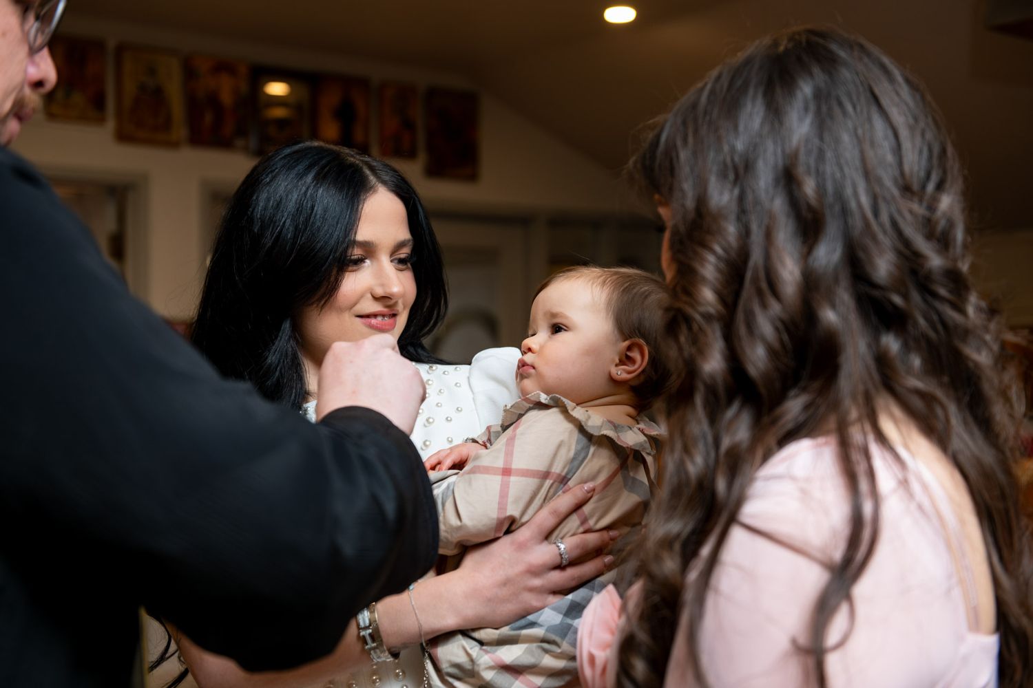Woman holding baby at a christening gathering while guests admire the infant.