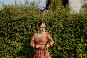 Traditional Indian bridal lehenga in deep red and gold embroidery photographed against lush green garden backdrop.