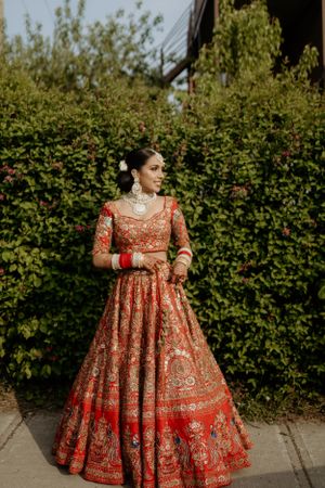 Ornate red and gold lehenga with intricate embroidery details showcased in outdoor garden setting.